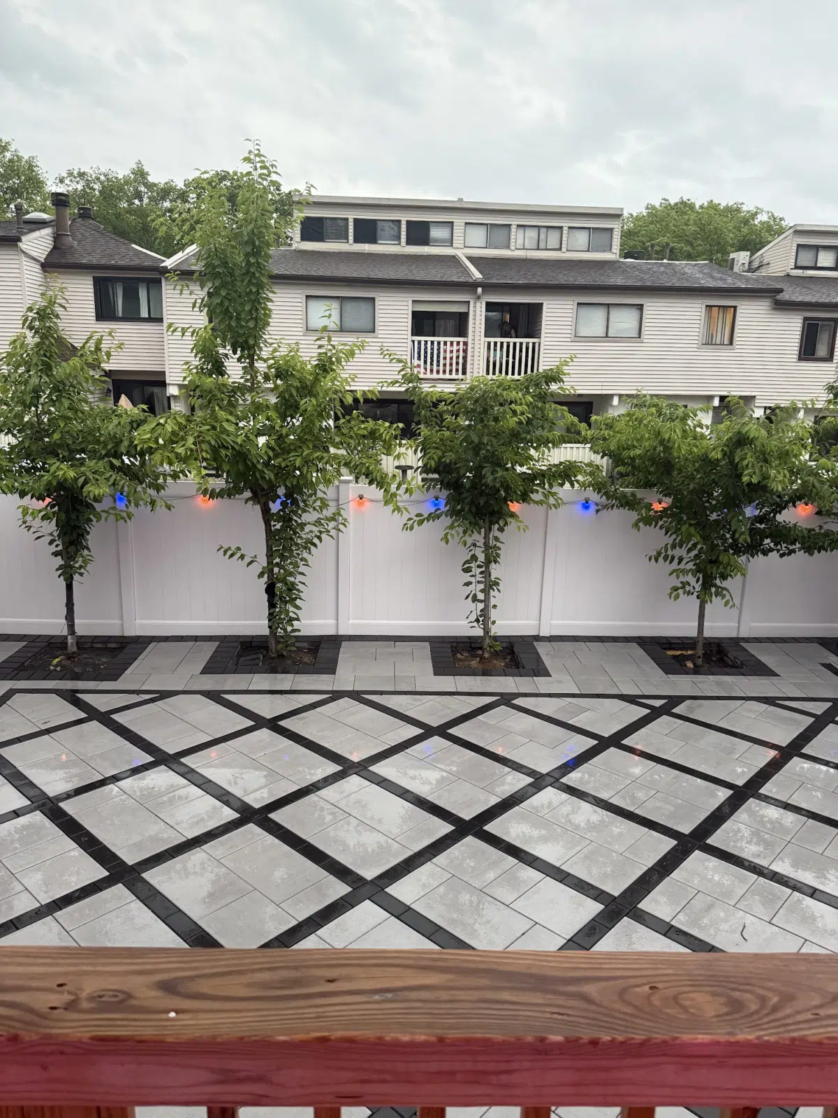 Gray paver patio with diamond pattern behind white fence and trees — APPLE MASONRY INC in Brooklyn